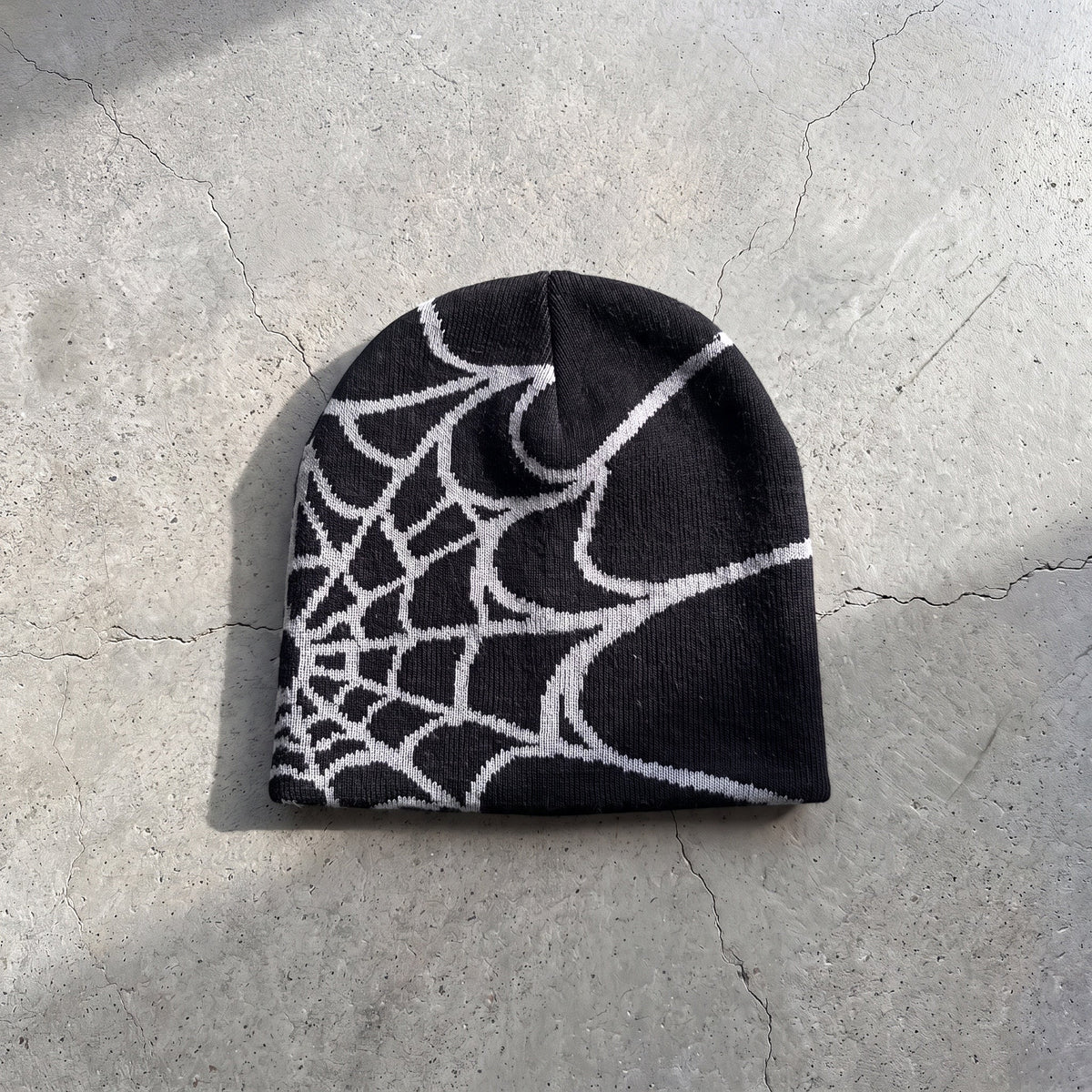 Black web knit beanie with bone white web on raw concrete